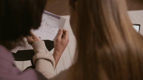 Over-the-shoulder shot of young couple reviewing bills and finances with laptop while sitting on sofa in apartment, multitasking at home in modern, cozy, and relaxed living space - Powered by Shutterstock - Get 15% off with code: PIKWIZARD15