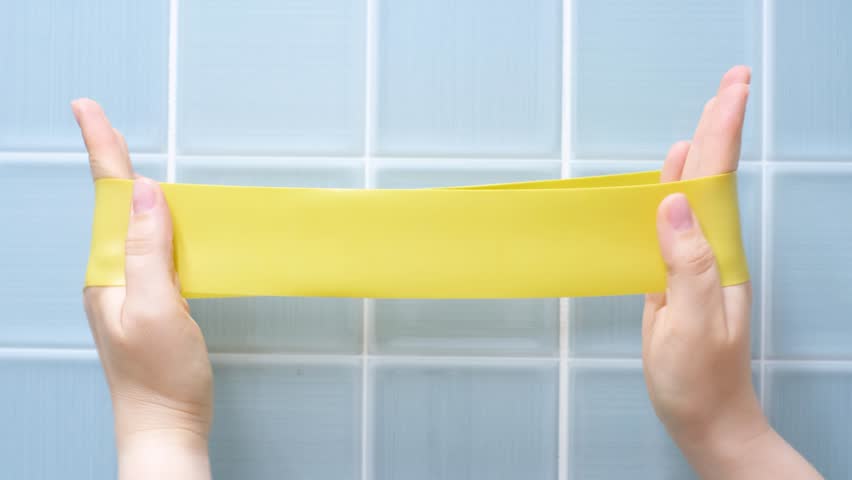 Hands stretching fitness elastic band against background of blue tiles.