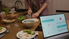 Young Caucasian couple enjoying breakfast at cozy home kitchen chatting with woman using calendar widget on laptop and man cooking warm meal in relaxed morning atmosphere - Powered by Shutterstock - Get 15% off with code: PIKWIZARD15