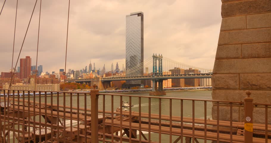 The pedestrian walkway of the Brooklyn Bridge, looking across the East River to the Manhattan Bridge and the Lower Manhattan skyline, featuring modern towers and river.