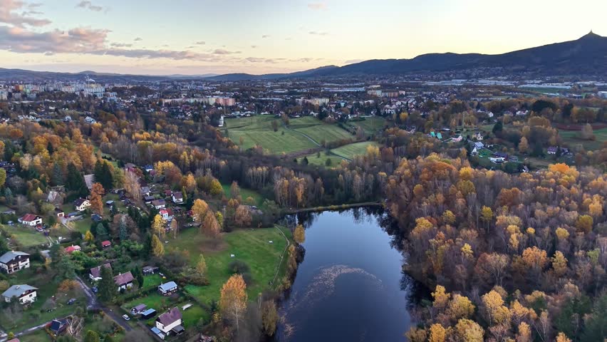 twilight hue reflects on peaceful pond, serene sunset view with lush fields and distant settlements