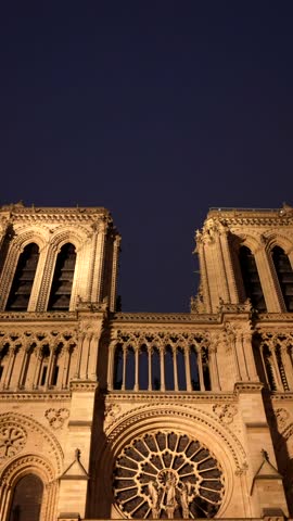 Low angle view moving down the magnificent western facade of the historic notre dame cathedral, beautifully illuminated against the dark parisian night sky, revealing its intricate gothic details