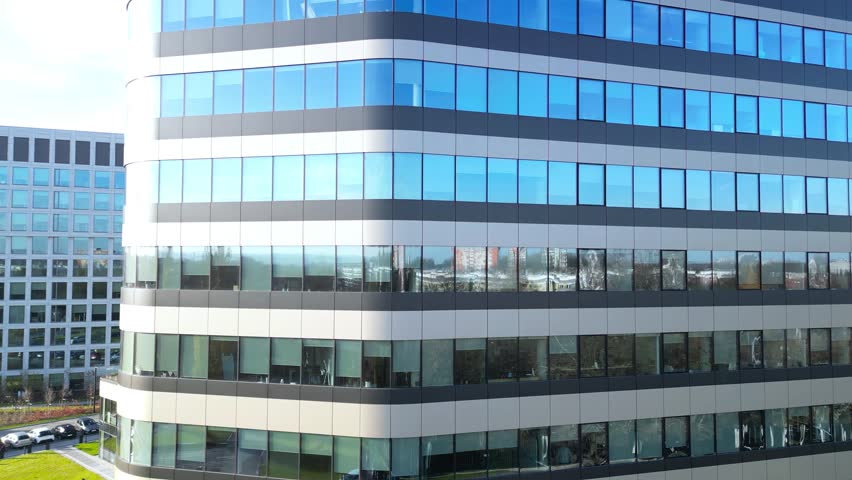 Modern office building exterior showcasing sleek glass facade, with reflections of the sky and surroundings, captured through a dynamic camera dolly movement emphasizing architectural design