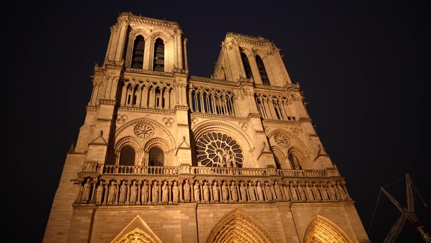 Low angle view of the illuminated facade of notre dame cathedral in paris, france, showing the intricate details of the gothic architecture against the dark sky after the 2019 fire