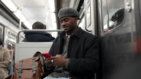 African american man wearing a beret sitting in a public transport wagon, browsing social media on his smartphone while commuting to work, enjoying the quiet journey through the city - Powered by Shutterstock - Get 15% off with code: PIKWIZARD15