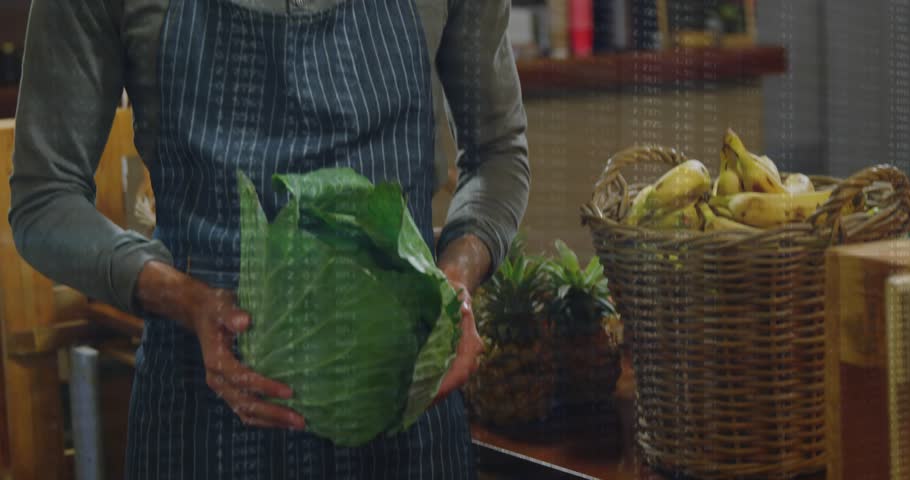 Camera panning, vendor checking cabbage freshness, raising head smiling with scanlines overlaying. Market, produce, retail, bananas, pineapples, apron, beard