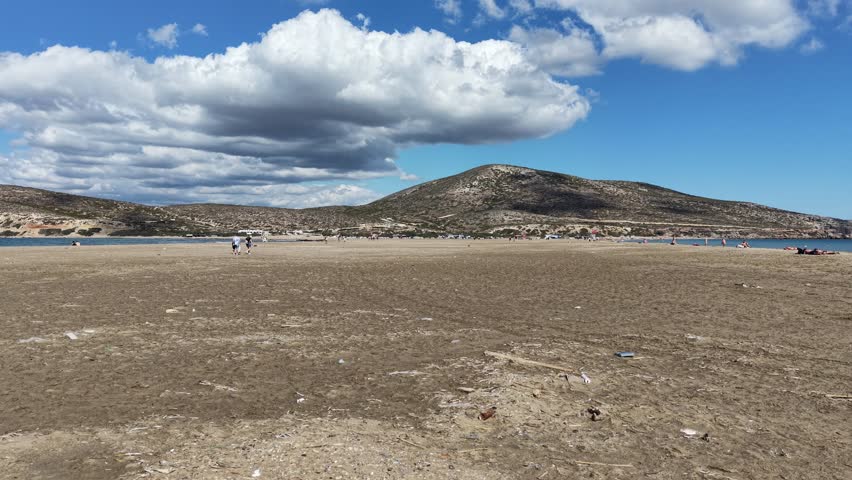 Aerial footage showcases a picturesque sandbar beach with distant hills in Elafonissi, Crete. The scene is captured under a partly cloudy sky, highlighting the natural beauty and tranquility.