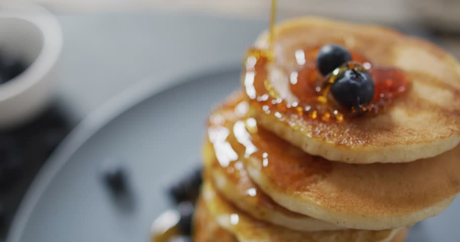 Syrup stream striking top pancakes, cascading syrup glossing layers with animated golden streaks. Blueberries, stack, breakfast, kitchen, tabletop, maple, bokeh