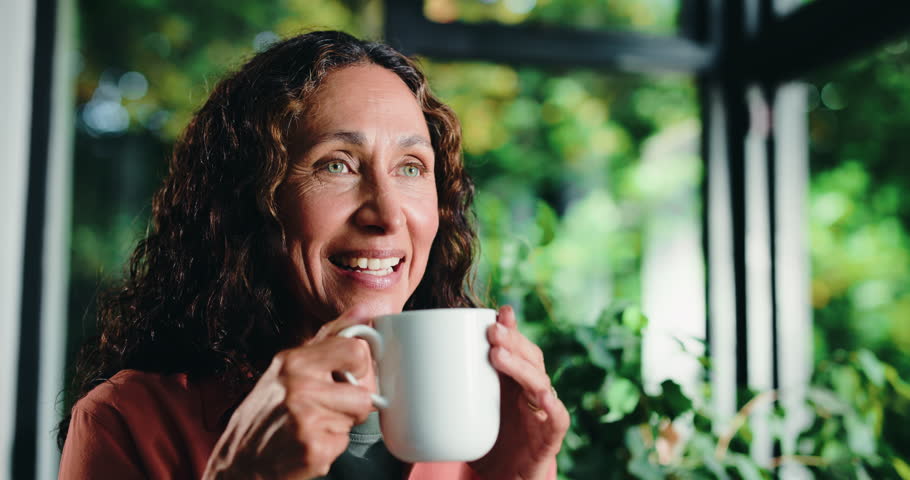 Coffee, smile and thinking with woman in home conservatory for contemplation or reflection. Drink, inspiration and relax with happy mature person in green sunroom for nostalgia or perspective