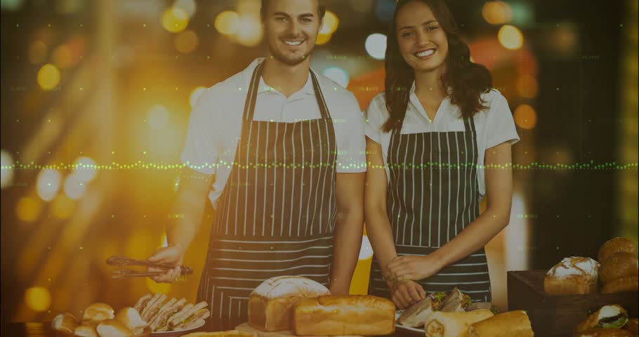 Two bakery staff at counter, audio-triggered green wave pulsing across torsos smiling for marketing. Pastry, bread, display, duo, warmth, glow, bokeh