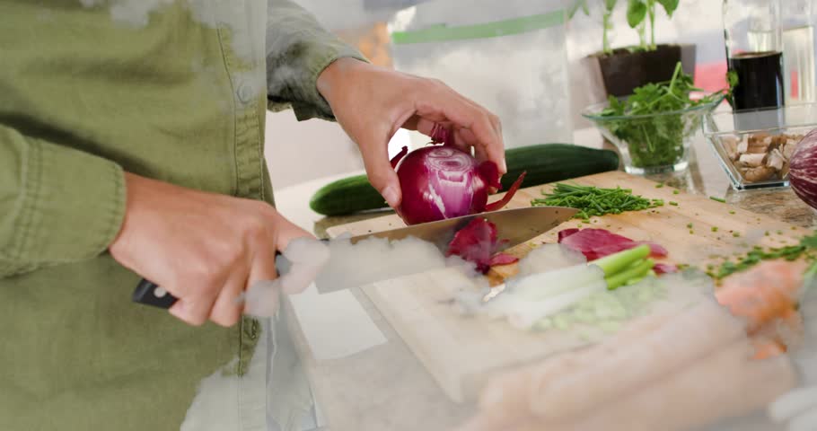 Woman prepping red onion in cooking scene, gripping chef's knife and peeling layers for meal prep. Kitchen, vegetables, cucumber, mushrooms, herbs, cuttingboard, chopping