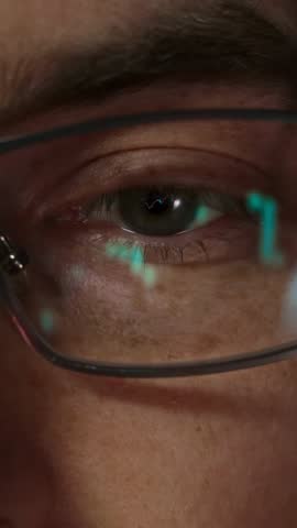 Close-up of a male trader eye with candlestick charts and financial graphs reflecting in his eyeglasses, symbolizing intense market analysis and crypto trading. Vertical video