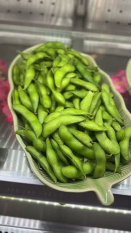 close-up vertical video of green edamame pods arranged on leaf-shaped plate in bright display