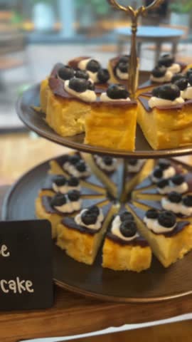 vertical video of cheesecake slices with blueberries and cream arranged neatly on tiered tray