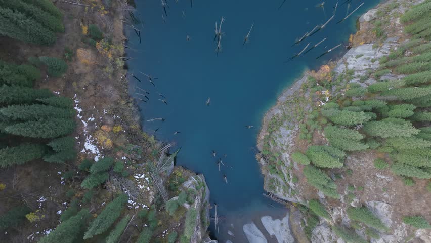 Aerial perspective captures a tranquil lake with submerged trees, showcasing vibrant colors and reflections. The camera pans and zooms, revealing the depth and beauty of the scene
