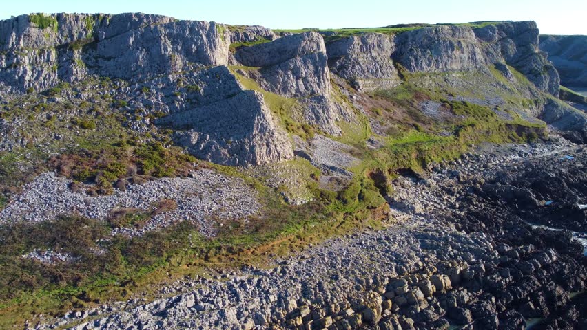 Aerial Overview Along Welsh Coastline with Eroding Grass Banks and Rock Formations with Coastal Path at Top. Beautiful Gower Peninsula Tourist Destination.