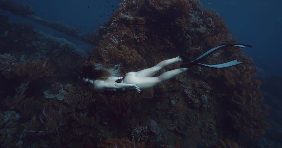 Freediver woman glides underwater in blue ocean on Japanese wreck in Bali