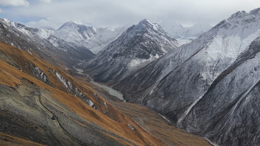 Majestic mountain landscape showcases snow-capped peaks and rugged terrain, as the camera pans across the scene, revealing the beauty of nature and the vastness of the valley below