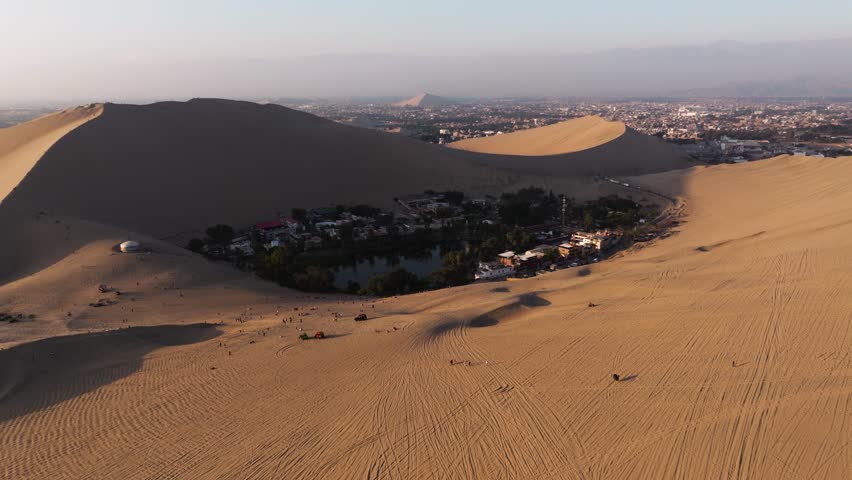 Buggy trails cut through sandy hills creating dynamic lines across the open Huacachina desert leading to oasis and neighborhood