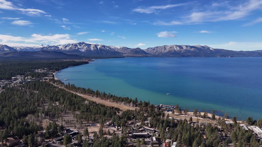 Aerial panoramic view of South Lake Tahoe coastline and town with snowy mountains