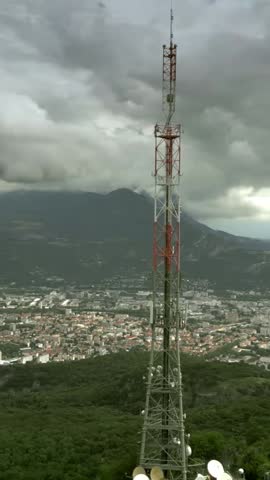 Aerial view of the telecommunication tower with many antennas against the cityscape of Grenoble. France, vertical video