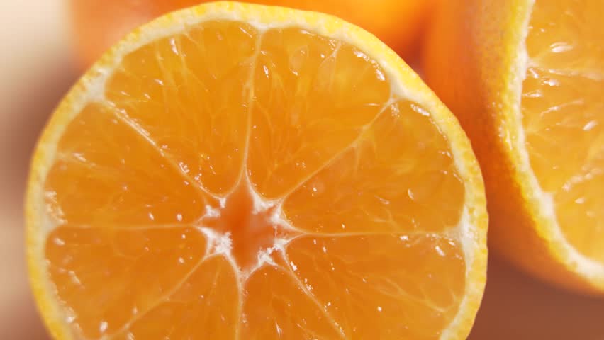 Macro mandarin cross-section rotates, showing juicy segments and translucent pulp. Warm studio light and soft background emphasize texture.