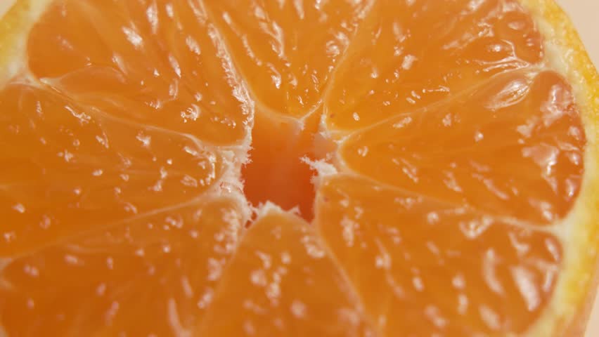 Extreme close-up of a mandarin half rotates, focusing on the center and juicy membranes. Glossy pulp and rind texture fill the frame.