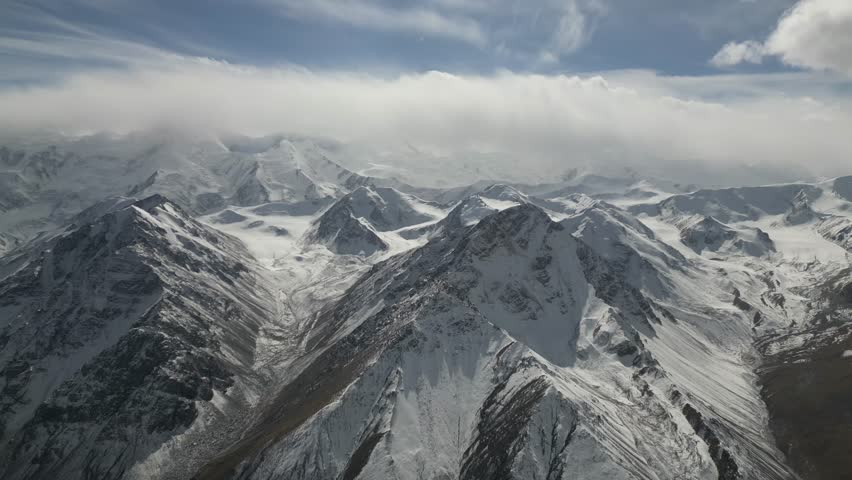 A breathtaking view of a snow-capped mountain range unfolds as the camera smoothly pans across the landscape, revealing the majestic peaks and valleys under a bright sky, showcasing nature