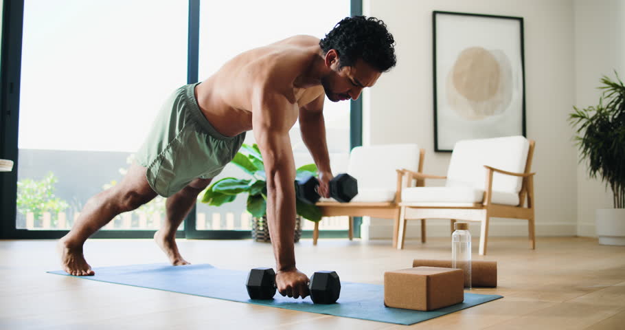 Man, fitness and weightlifting with dumbbells in home for exercise, muscle gain or training. Active, muscular or male person with equipment or weights for arm workout or renegade row on mat in house