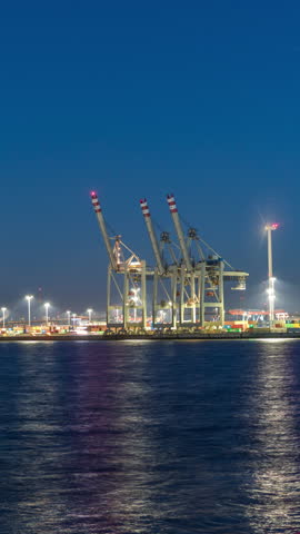 Night timelapse of Hamburg cargo port, showcasing container terminals, cranes and cargo ships on the Elbe River. Boats and vessels pass by, creating a dynamic maritime panorama. Germany
