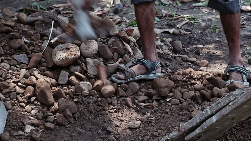 An adult Indian worker breaks stones manually using tools at an outdoor construction site. The scene highlights physical labor,traditional methods, and everyday construction work in India
