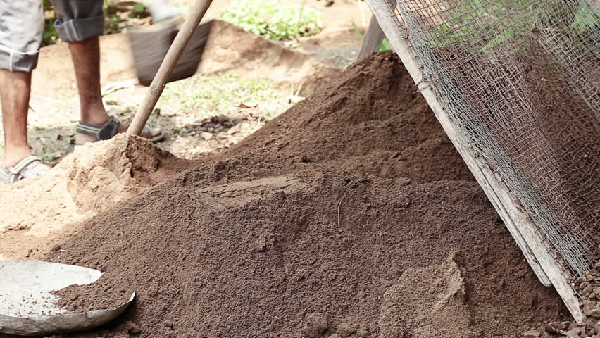 Adult Indian men mix soil manually using tools during outdoor construction work. The scene highlights physical labor, teamwork, traditional methods, and everyday building activity in India.
