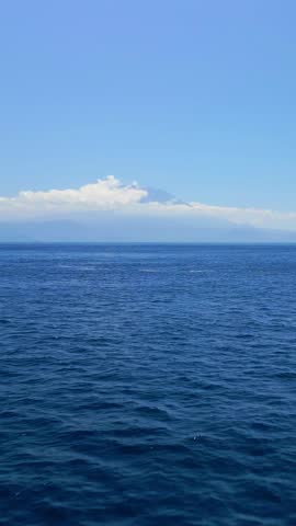 Fast aerial flyover from Nusa Penida toward Bali with cloud-covered Mount Agung on the horizon, captured in high quality for conceptual travel promo, tourism advertisement and cinematic ocean