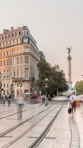 Triangular building and modern tram at Place de la Comedie timelapse, Bordeaux, France, during sunset. Shadow move across the facade and a streetlight with a clock adds elegance to this urban landmark