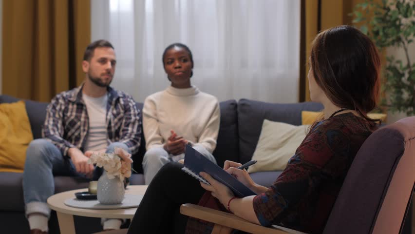 Young multiracial couple discussing relationship problems with a female psychologist at a therapy session
