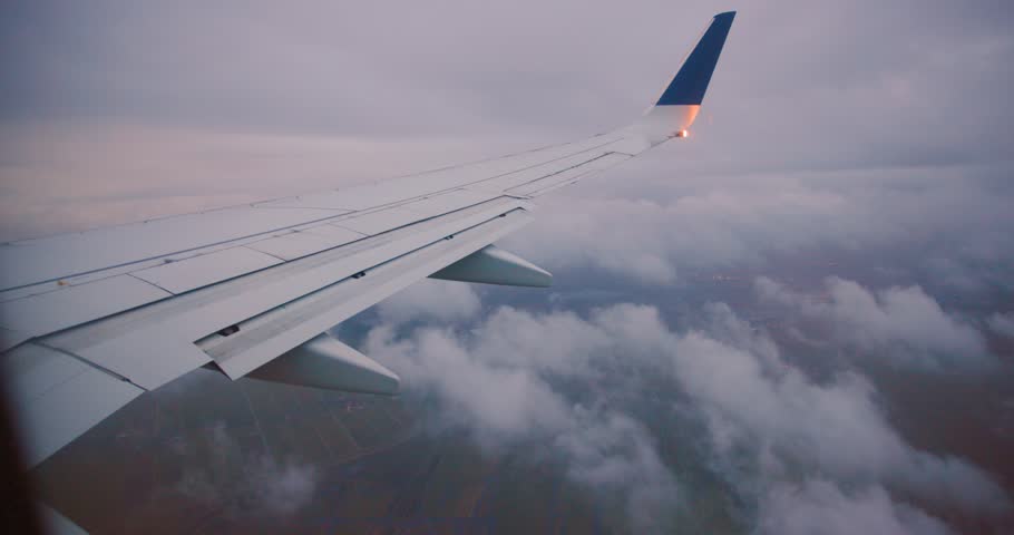 Passenger view from an airplane window showing the wing flying over a sea of clouds. A beautiful, serene sunset colors the horizon