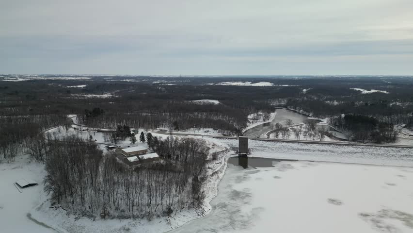 Flying forward over a frozen lake in Iowa, the Coralville Reservoir. It is a destination for recreation in the region. The dam and road across are looking south towards Iowa City. 4k drone winter