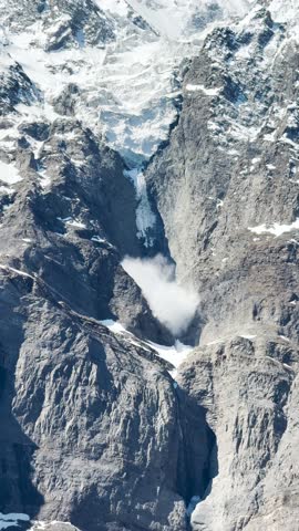4K Vertical shot of Sluff avalanche due to the piece of Glacier falling from the top of the Himalayan mountain of Tinnan valley in Lahaul, Himachal Pradesh, India. Global warming background. 