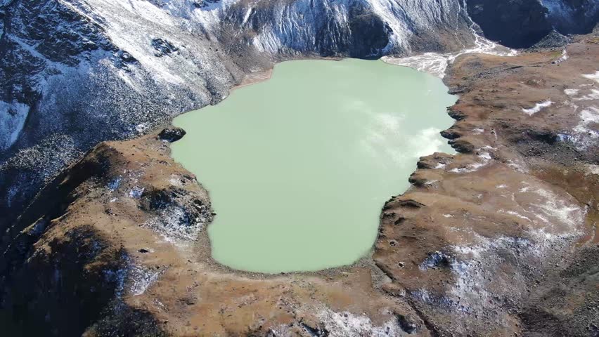 Cinematic aerial top-down shot of Lake Syltrankel surrounded by rugged mountains. Crystal-clear turquoise water, rocky shoreline and untouched wild nature create a calm and dramatic atmosphere.