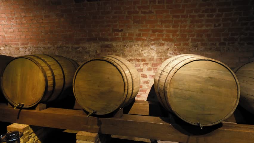 Antique wine cellar with wooden racks holding a collection of empty green glass bottles and a large oak barrel, showcasing a rustic and historic atmosphere for winemaking and storage