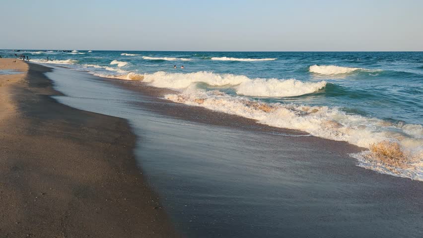 Sea waves shimmer on the sand in afternoon light.