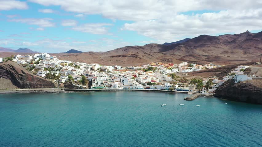 Drone footage capturing La Playita, Fuerteventura, highlighting the serene beach, crystal-clear ocean, and picturesque village streets. Ideal for lifestyle, travel, and scenic background content.