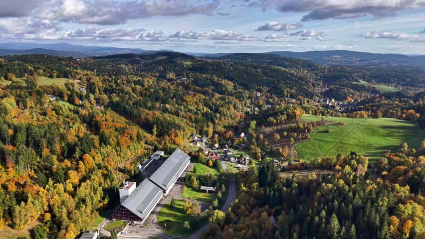 Aerial Rural Complex With Large Facility Roof, Rolling Autumn Hills, Forest Edges And Open Fields Under Clear