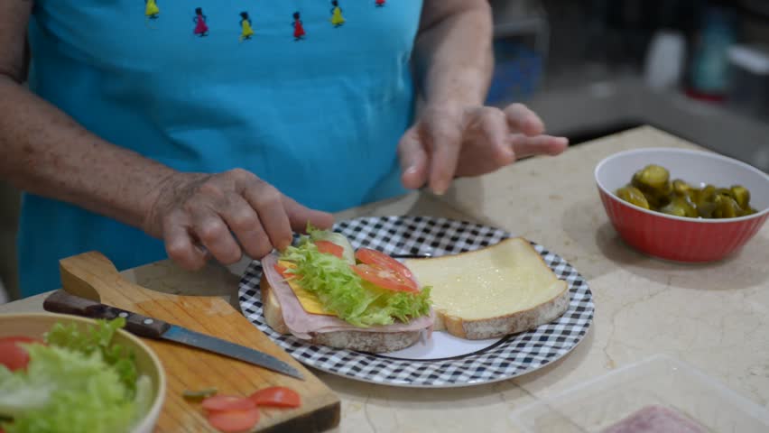 Elderly woman preparing a sandwich, close-up of her hands.