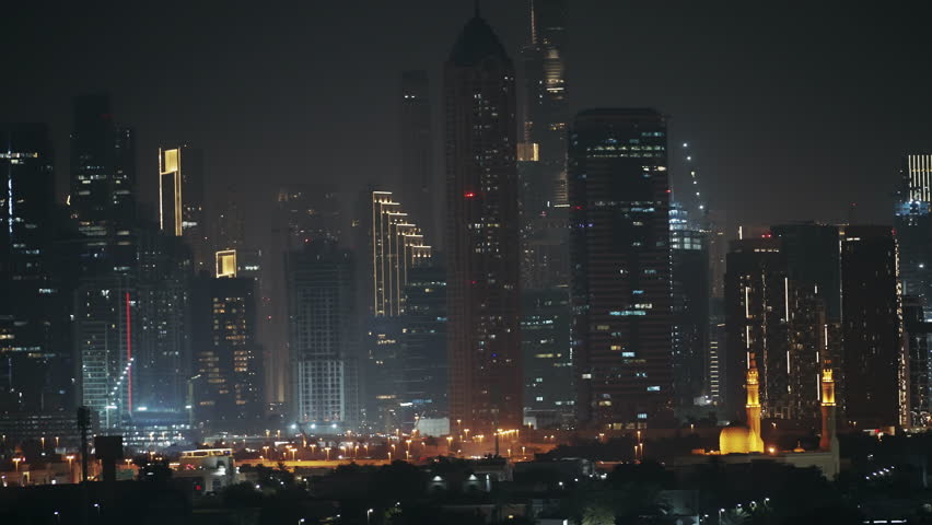 Panoramic view of Dubai at night showcasing modern skyscrapers and a beautifully lit mosque in the foreground