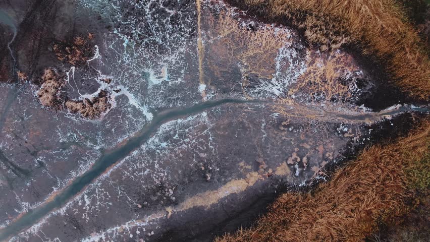 Drone flight up above the Milice ponds Gądkowice, Poland, winter, autumn, raw, wild nature, dried up, frozen, abstract cracks of ice and water from above in the moody cinematic style