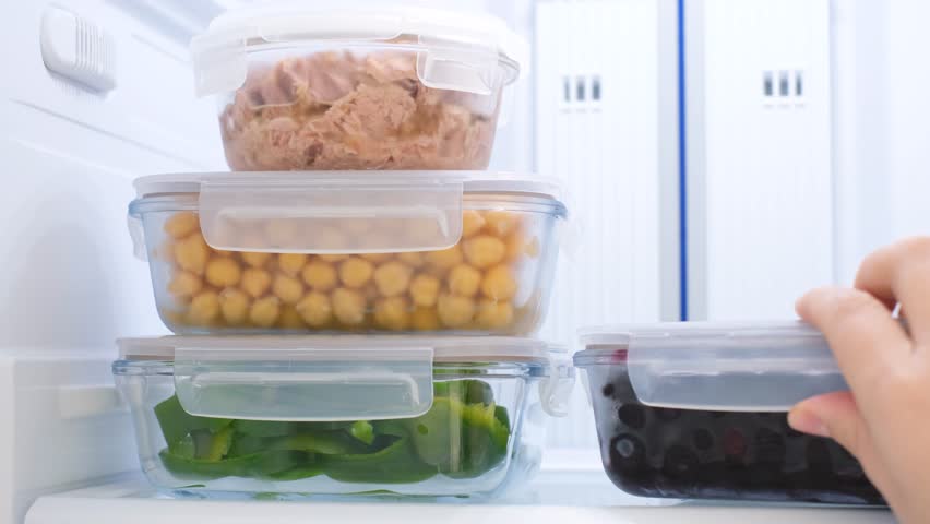 A hand takes glass box of frozen blueberries out of the refrigerator.