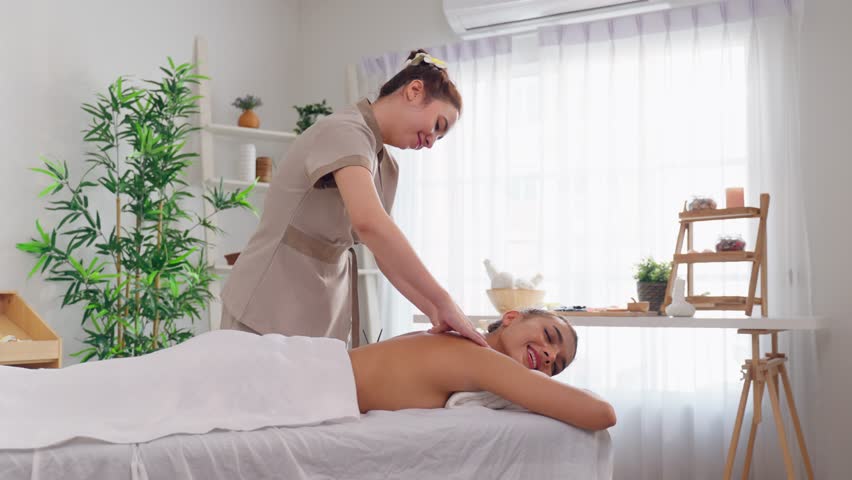 Beautiful woman getting back massage treatment with oil at beauty spa. Attractive young girl lying down on massage bed getting relaxing physiotherapy service from masseuse for body in spa clinic.
