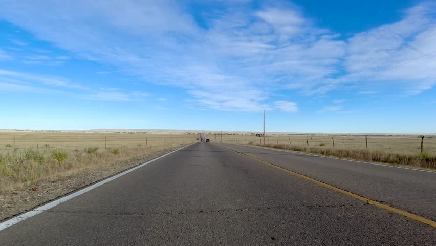 Driving west looking back towards the east in this rearview perspective.  Straight road with telephone poles and a wood fence pass.  Blue winter skies of the high desert and empty roads.
