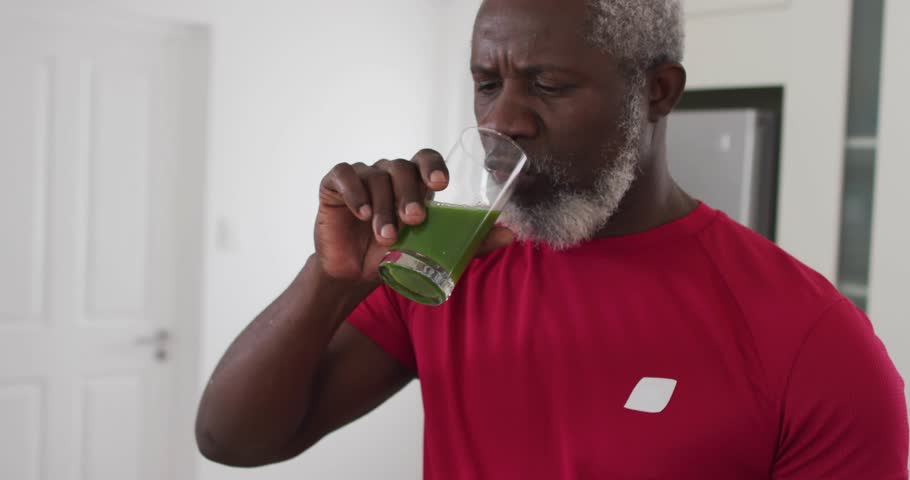 Man raising glass to lips, tasting green-liquid by doorway while tech HUD staying fixed to camera. Minimalist, hallway, contemporary, overlay, analytics, hydration, residential
